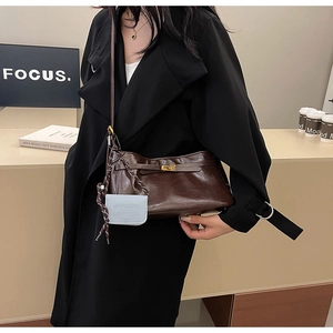 Detail of dark brown glossy leather bag with gold buckle and blue MUCOOU pendant