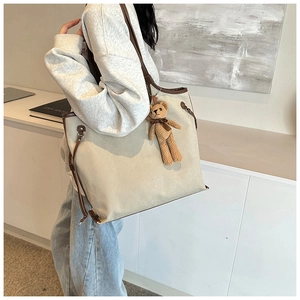 Detail of canvas tote bag with leather trim and brown knit bear charm accessory