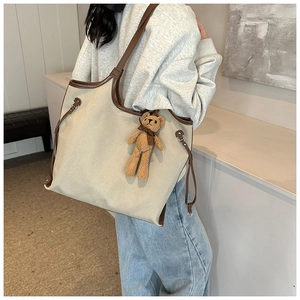 Detail of canvas tote bag with brown leather straps and a cute plush bear charm