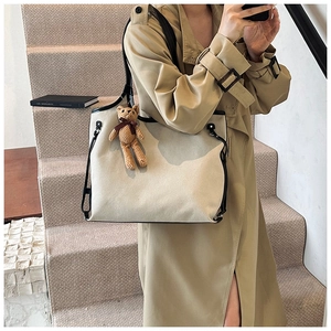 Detail of off-white canvas tote bag featuring black trim and cute brown plush bear charm
