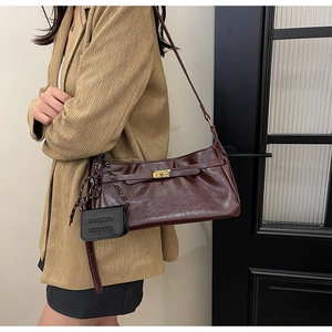 Detail of dark red textured leather shoulder bag with golden lock and mini charm