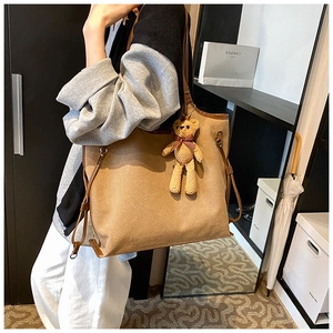 Detail view of camel tote bag with brown leather trim and a cute woven bear charm