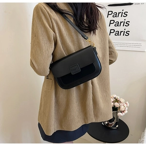 Detail of minimalist black matte leather crossbody bag with elegant gold hardware on model