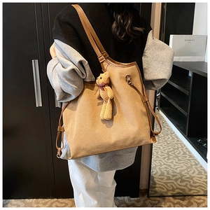 Back view of a khaki canvas tote bag with brown leather straps and a plush bear charm