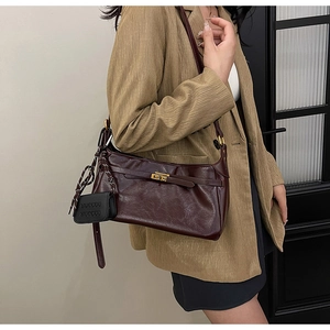 Detail of dark burgundy textured leather shoulder bag with gold twist lock on model