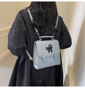 Détail d'un sac à dos en similicuir bleu clair avec patch chat noir et boucles