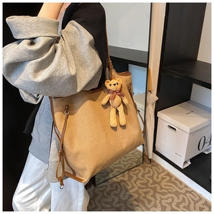 Detail of canvas tote bag with brown leather trim and a cute knitted bear charm