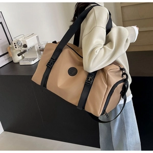 Detail of camel cylindrical sports bag with wide black straps and circular logo detail