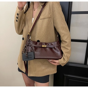 Detail view of burgundy leather shoulder bag featuring a metallic lock and mini pouch charm