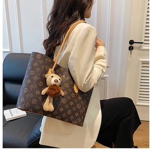 Detail of a brown leather tote bag with pattern and a decorative teddy bear charm