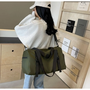 Detail of army green travel bag with sturdy handles and adjustable shoulder strap worn by model