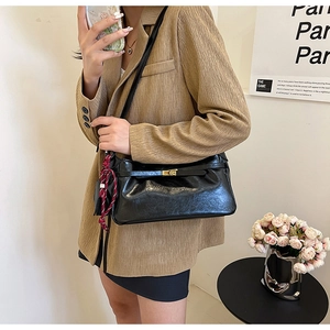 Glossy black underarm bag featuring a gold buckle and silk scarf on a beige suit