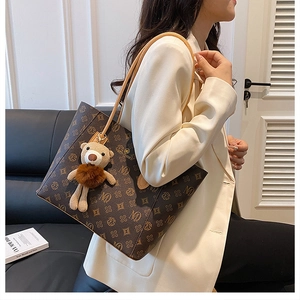 Detail of vintage tote bag featuring floral monogram pattern and a teddy bear charm