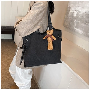 Large black tote bag with brown teddy bear charm shown on model in a modern room