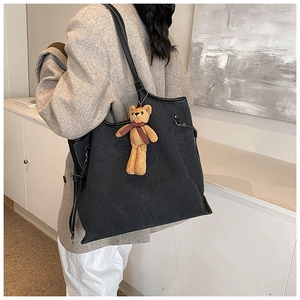 Close-up of a large grey fabric tote bag with black leather straps and a bear charm