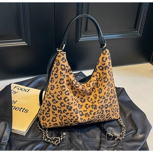 Detail of leopard print tote bag with gold chain strap on black leather jacket background
