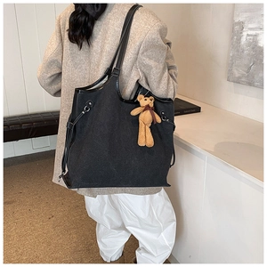 Detail of large black canvas tote bag with leather trim and bear pendant on model shoulder