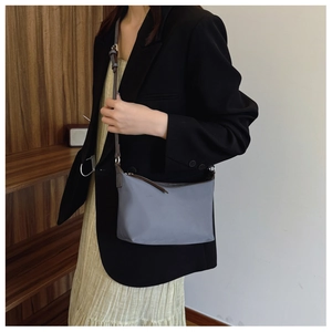 Gray-blue nylon crossbody bag with slim brown strap worn by a model in a cozy setting