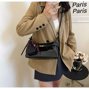 Detail of black glossy leather shoulder bag with gold clasp and decorative charms