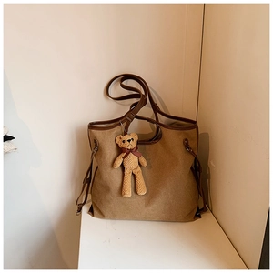 Detail of khaki canvas tote bag featuring brown leather trim and cute knit bear charm
