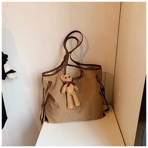 Close-up of a brown canvas tote bag with leather trim and a cute knitted bear charm