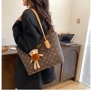 Detail view of large brown monogram tote bag with shoulder strap and plush bear charm