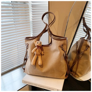 Detail of khaki canvas tote bag featuring brown leather trim and cute knitted bear charm