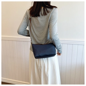 Detail of navy nylon shoulder bag with brown leather strap shown on a model
