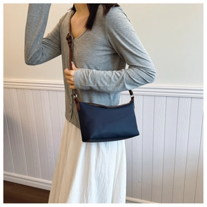 Detail of navy blue water-resistant bag with adjustable brown leather shoulder strap