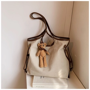 Detail of canvas tote bag with brown trim and small teddy bear charm on white book