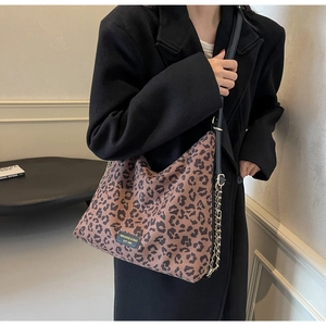 Detail view of leopard print tote bag featuring black leather straps and gold chain links