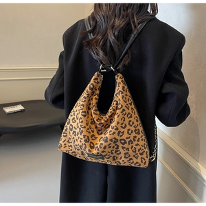 Detailed view of leopard print shoulder bag worn over a black coat in a modern interior
