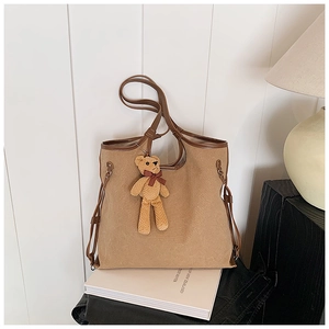 Detail of khaki canvas tote bag with brown leather trim and cute teddy bear pendant