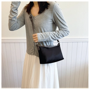Model wearing a black nylon crossbody bag with brown leather trim for casual commuting style