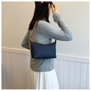 Detail of navy nylon baguette bag with brown leather trim and slim shoulder strap
