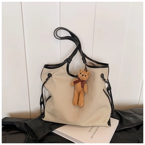 Detail view of large canvas tote bag with black leather trim and a cute knitted bear charm