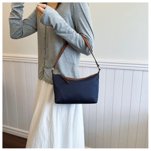 Side view of navy nylon shoulder bag with brown leather strap on model for size perspective