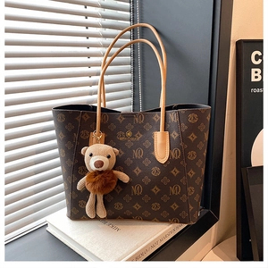 Detailed view of brown monogram tote bag with gold logo and plush bear charm on books