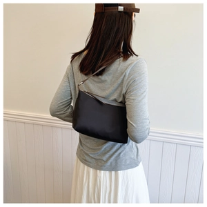 Detail of black nylon shoulder bag with brown leather strap worn by a model in soft light