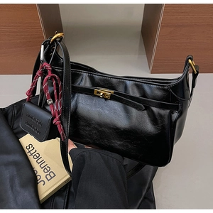 Detail of black glossy shoulder bag with gold twist lock and mini brand charm