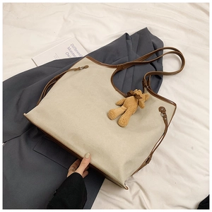 Close-up of canvas tote bag with brown leather handles and a plush bear pendant