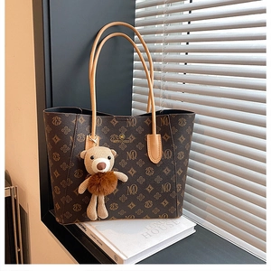 Detail of dark brown monogram tote bag with gold logo and plush teddy bear charm