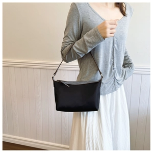 Close-up of minimalist black nylon shoulder bag with brown strap and silver ring detail