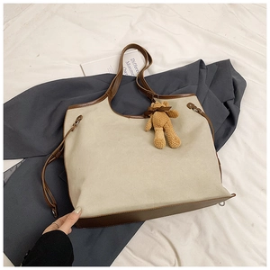 Detail of off-white canvas tote bag with brown leather trim and cute plush bear charm