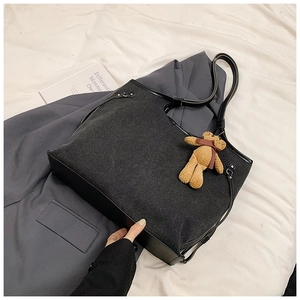 Close-up of large dark grey denim tote bag with leather handles and teddy bear charm