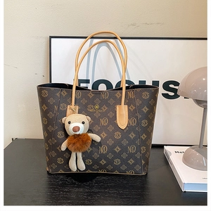 Detailed shot of dark brown monogram tote bag with plush bear charm and leather strap