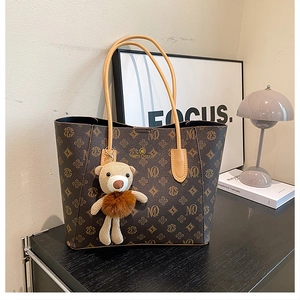 Detail of vintage brown leather tote bag with floral pattern and cute bear charm hanging