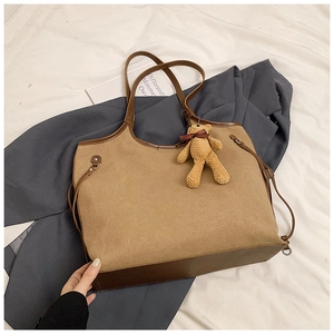Detail of a large khaki tote bag with a brown bear pendant on a grey blazer background