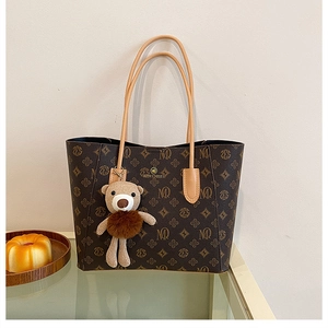 Macro detail of retro monogram tote bag with brown leather handles and a plush bear charm