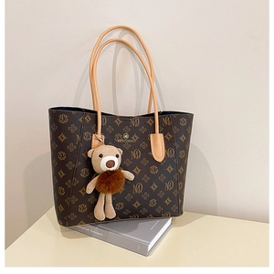Detail of vintage monogram pattern on brown tote bag with cute bear charm accessory